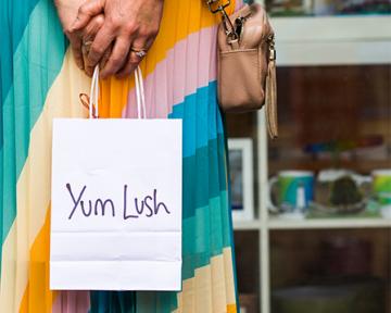 A lady wearing colourful text holding Yum Lush bag in her both hands